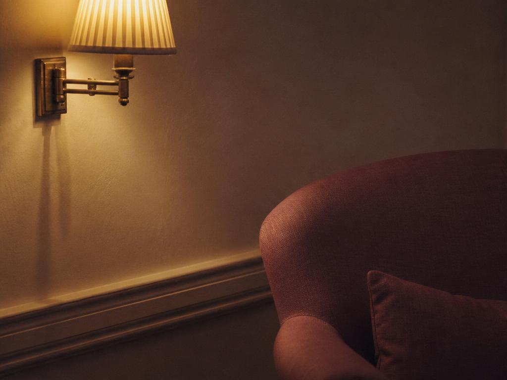 A lit wall lamp beside an armchair in a warm evening interior